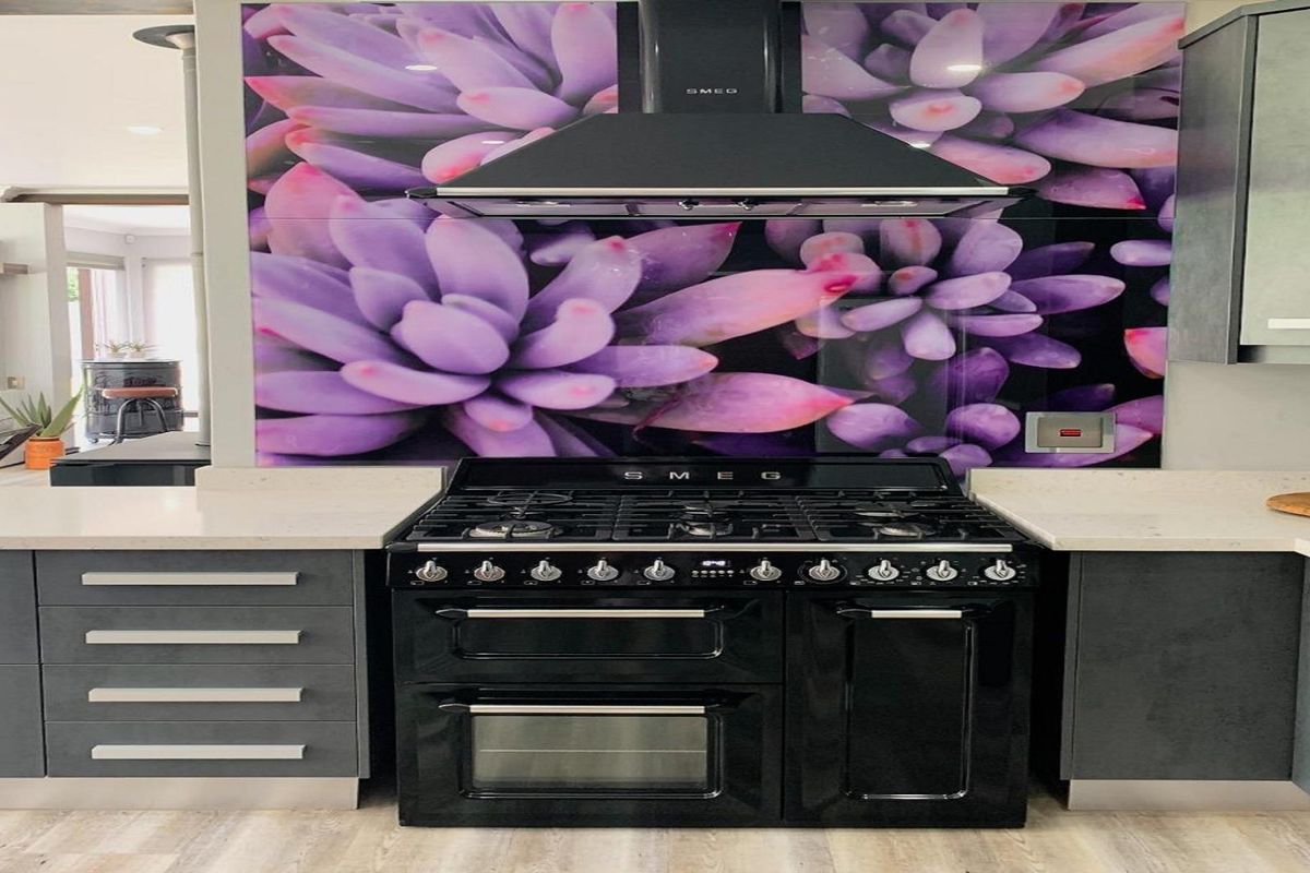 Modern kitchen featuring a high-end Smeg gas range cooker, extractor fan, and a striking floral-patterned glass splashback with stone countertops.