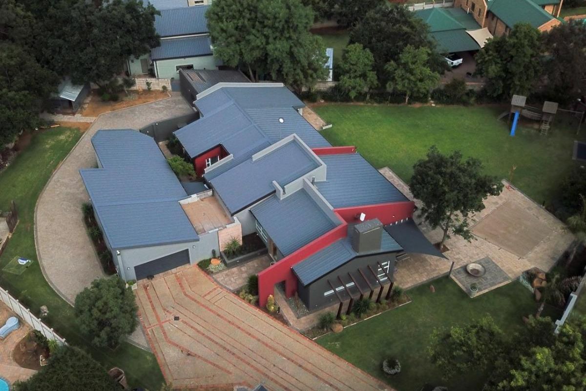 Aerial view of a modern residential property featuring a multi-pitched metal roof, paved driveway, expansive lawn, and integrated garage structure.