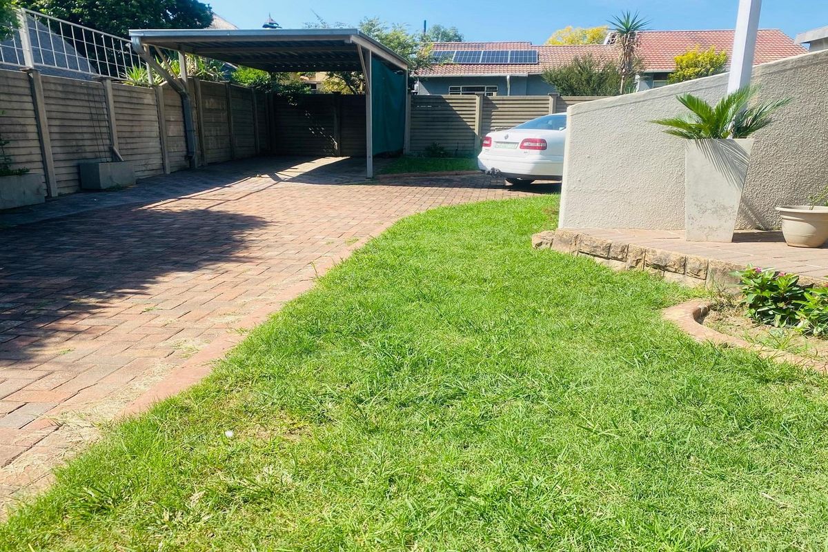 A paved driveway area featuring a covered carport, adjacent lawn, and perimeter boundary walling, providing functional off-street parking space.