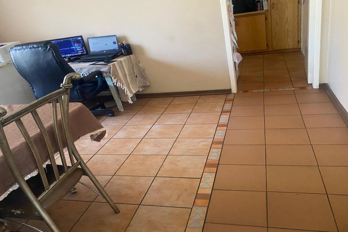 A view of a tiled living area with a transition strip leading into a hallway and kitchen area.
