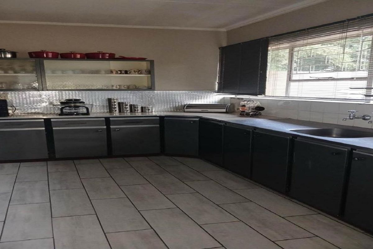 A functional kitchen featuring dark cabinetry, a stainless steel backsplash, tiled flooring, and a window with fitted blinds.
