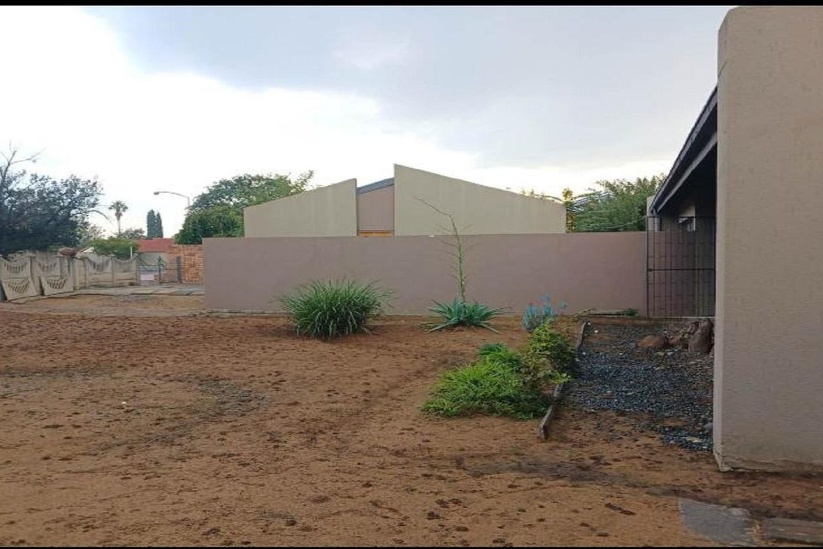 A view of the rear yard area featuring perimeter boundary walls and basic landscaping, offering potential for garden development.