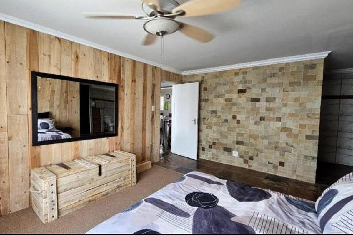 Bedroom featuring a timber-clad feature wall, stone-tiled accent wall, ceiling fan, and carpeted flooring.