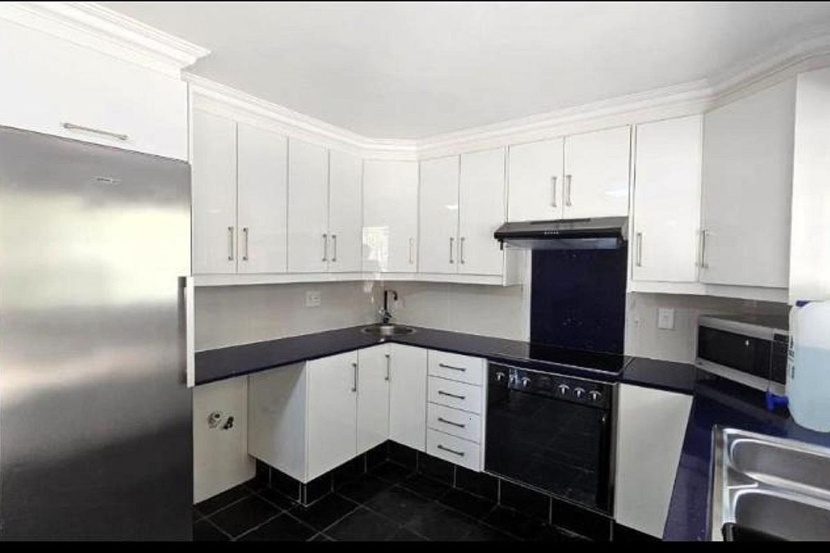 Modern kitchen featuring white cabinetry, dark countertops, a built-in oven with extractor fan, and tiled flooring.