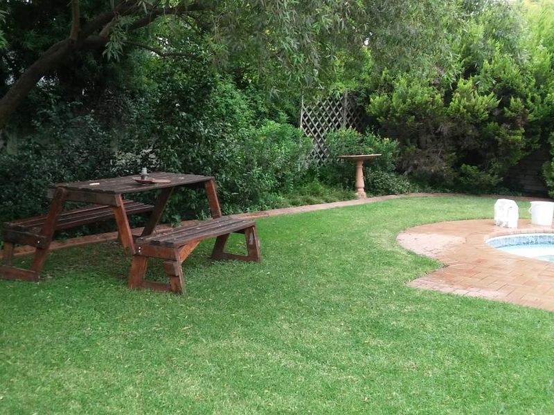 A private backyard featuring a swimming pool with brick coping, surrounded by a lush, mature garden and established trees.