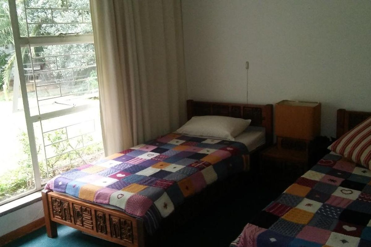 A bedroom featuring a large window with security bars, providing natural light and a view of the garden area.