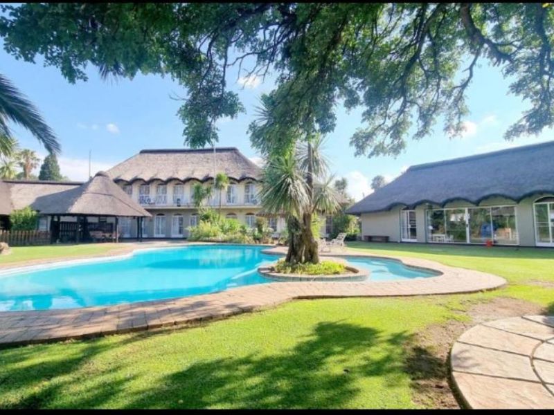 Spacious outdoor pool area featuring a large swimming pool, manicured lawn, and multiple buildings with traditional thatched roofs.