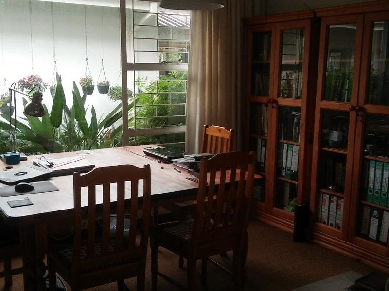 A home office space featuring built-in wooden shelving units and a large window with security bars overlooking a garden area.