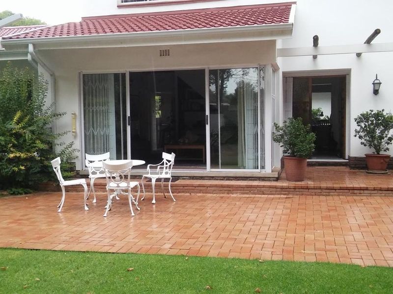 A paved outdoor patio area featuring a pergola, sliding glass door access to the interior, and a well-maintained garden setting.