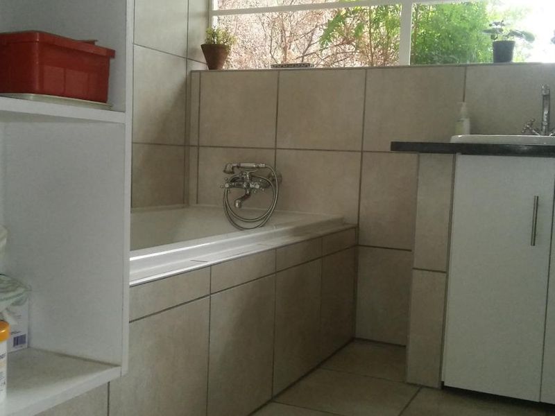 A functional bathroom featuring a built-in bathtub, vanity cabinet with basin, and neutral wall tiling with natural light from a high window.