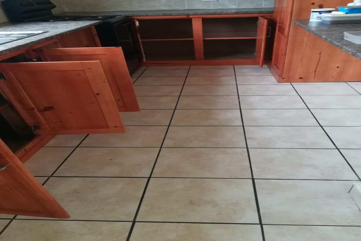 A kitchen area featuring wooden cabinetry, stone-look countertops, and tiled flooring, currently showing signs of wear and requiring maintenance.
