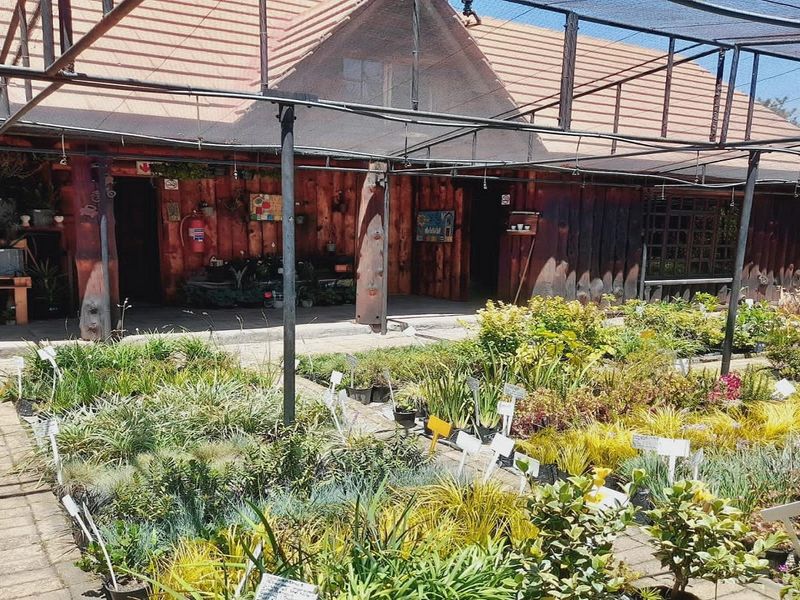 Exterior view of a rustic timber-clad building featuring a tiled roof and an extensive outdoor shade-covered nursery or garden area.