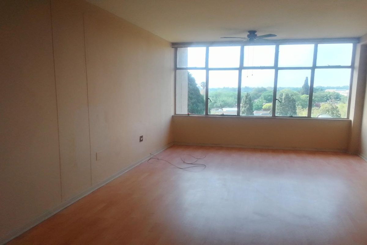 A spacious, empty living room featuring large windows with natural light, a ceiling fan, and wood-look flooring, offering a bright and versatile living space.