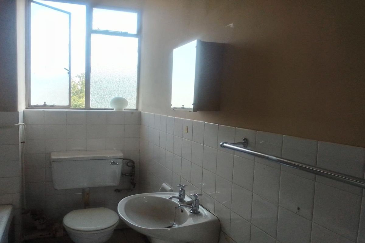 A dated bathroom featuring a standard toilet, pedestal basin, and wall-mounted medicine cabinet with tiled splashbacks and natural light from a window.
