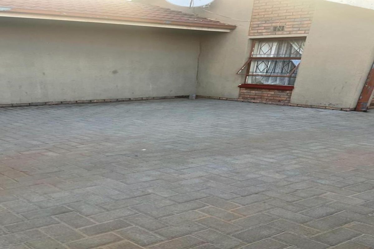 A paved rear courtyard area featuring brick and plastered wall finishes with security-barred windows.
