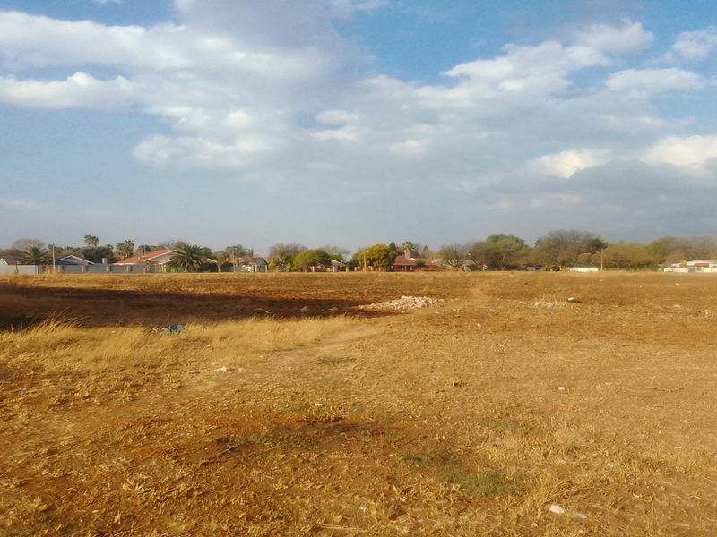 A wide-angle view of a vacant residential plot of land, featuring level terrain and surrounding neighborhood development.