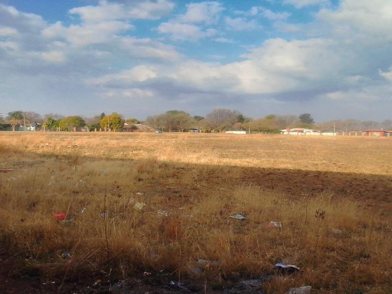 A wide-angle view of a vacant residential plot featuring dry, overgrown grass and open land, suitable for future development.