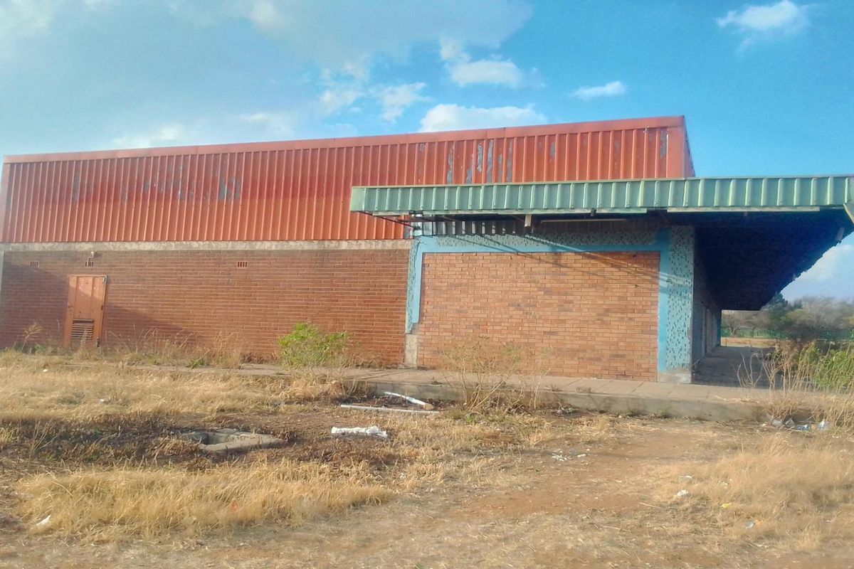 Rear view of a commercial-style building featuring brick masonry and corrugated metal cladding with a covered walkway, situated on a vacant plot.