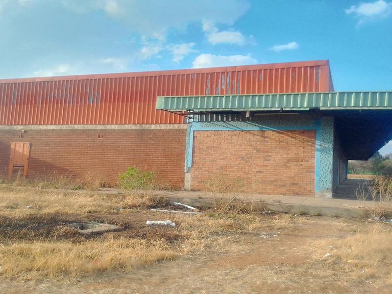 Rear view of a commercial-style building featuring brick masonry and corrugated metal cladding with a covered walkway, situated on a vacant plot.