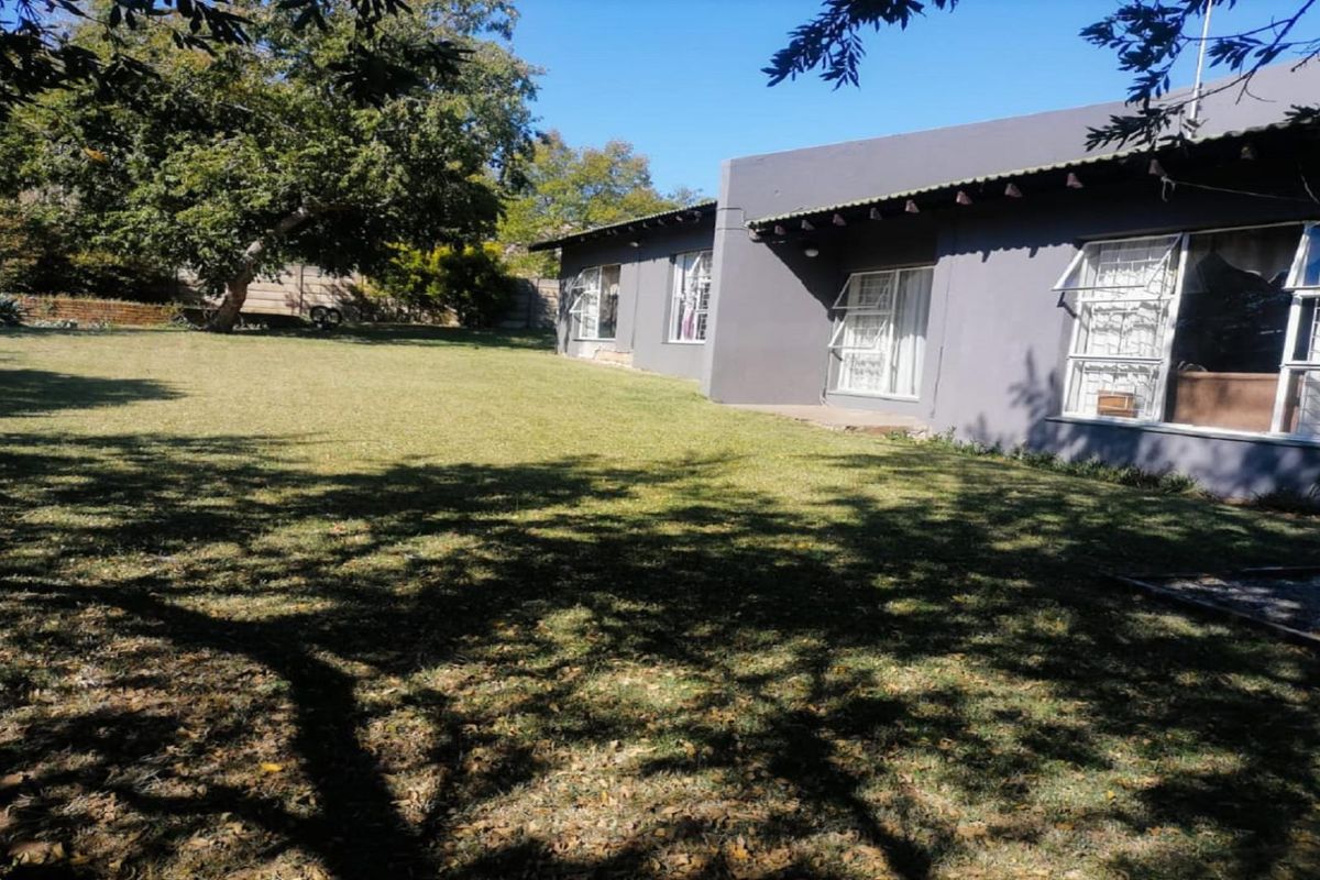 A spacious rear garden featuring a well-maintained lawn and a view of the property's rear elevation with large windows and security bars.