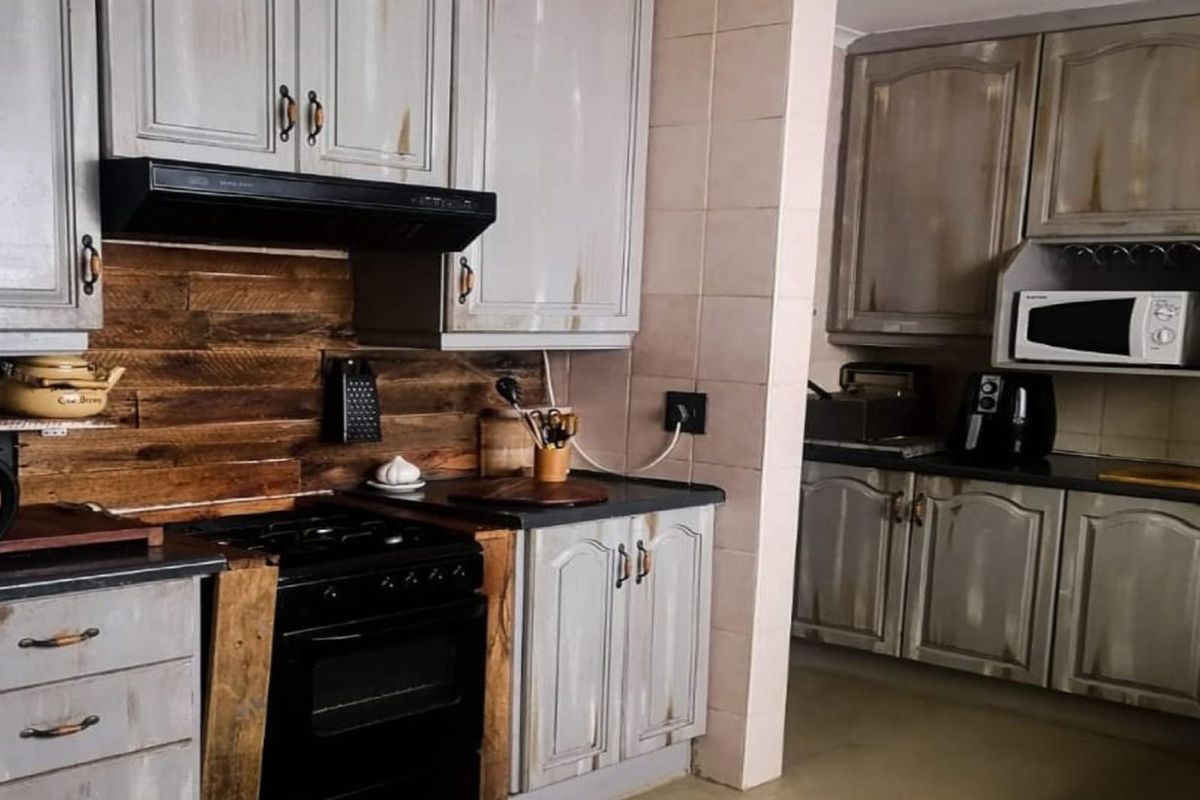 A rustic-style kitchen featuring distressed grey cabinetry, dark countertops, a built-in oven with extractor fan, and a timber-clad splashback.