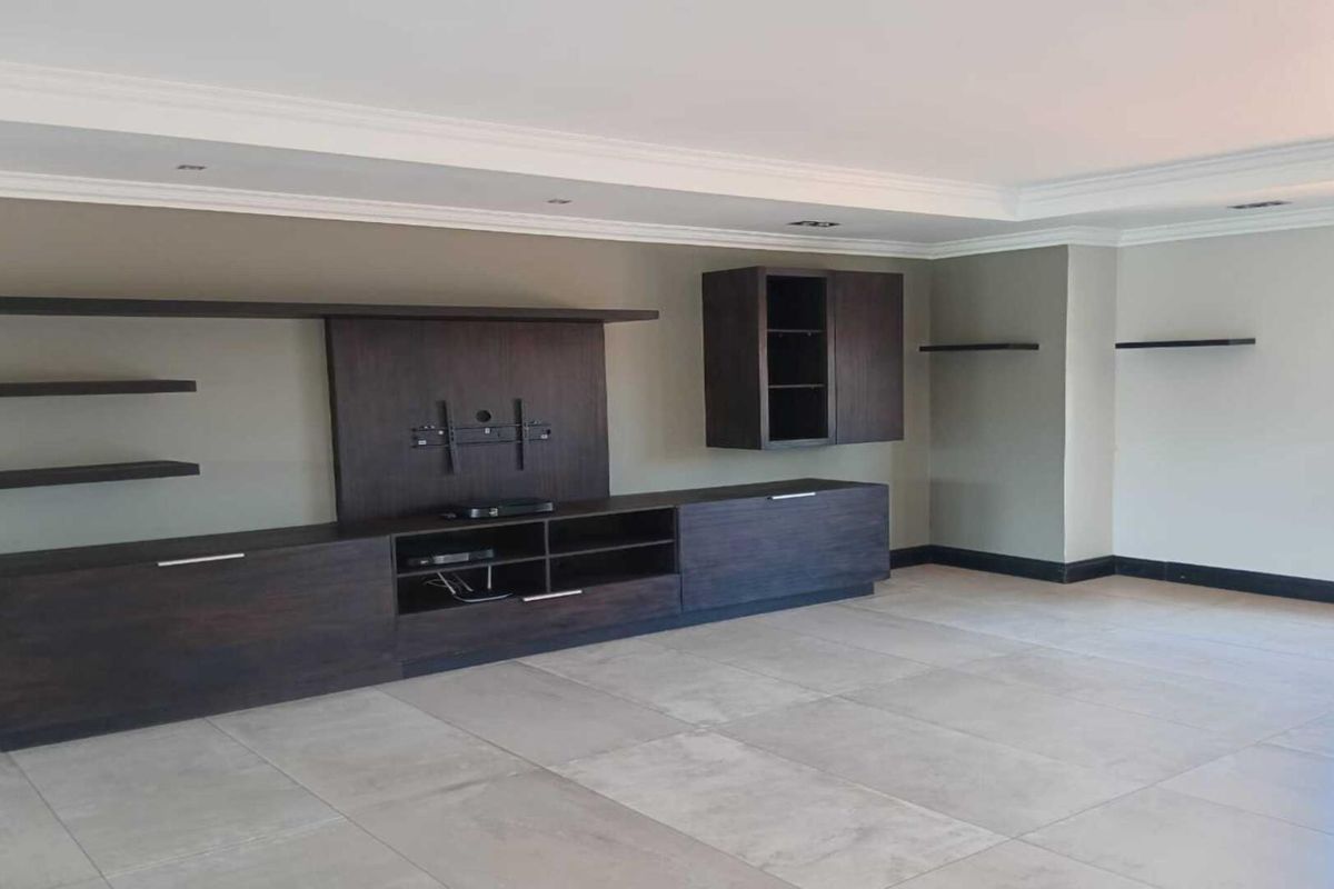 Spacious living room featuring large format floor tiles, crown molding, and a custom built-in dark wood media unit with integrated shelving.