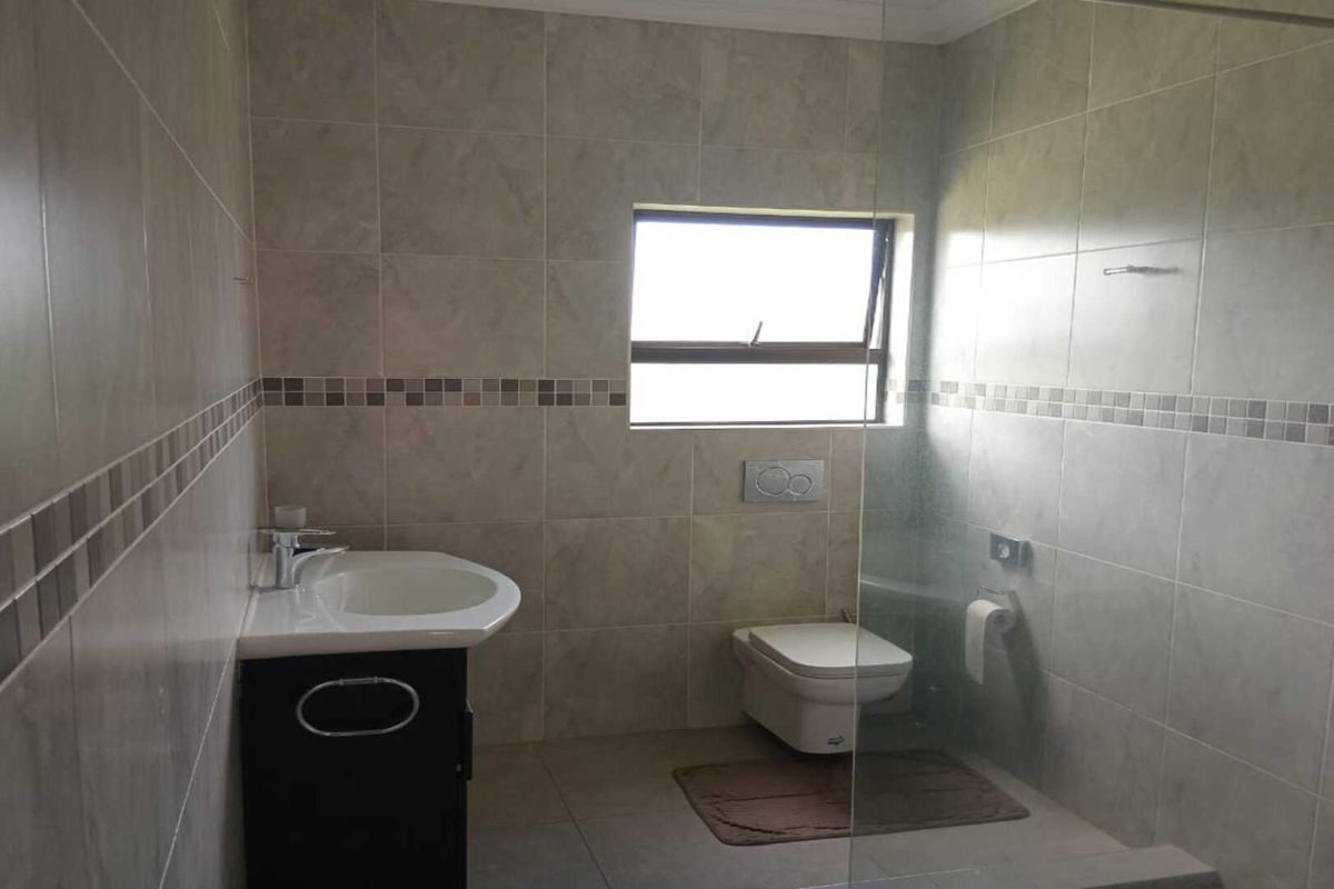 A modern bathroom featuring floor-to-ceiling neutral tiling, a wall-mounted toilet, a glass shower screen, and a vanity basin.