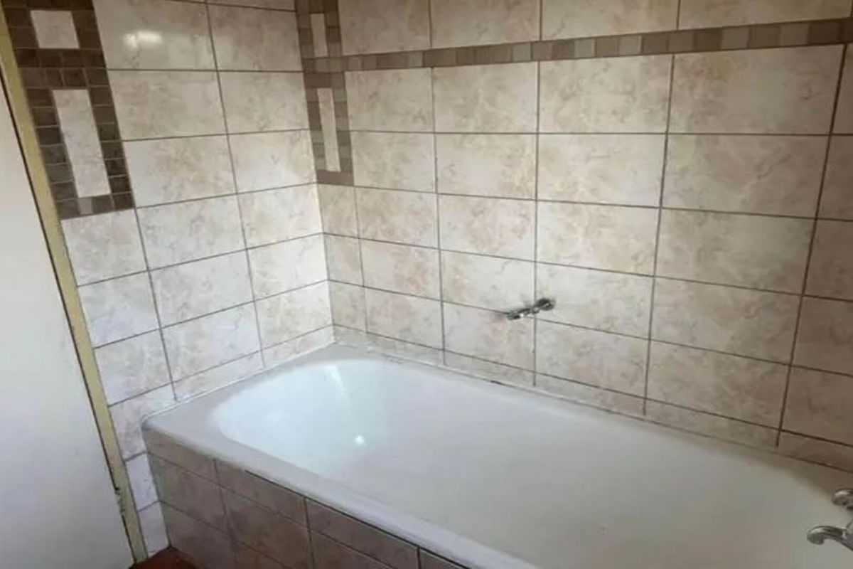 A functional bathroom featuring a built-in bathtub with tiled surround and wall-mounted faucet fixtures.