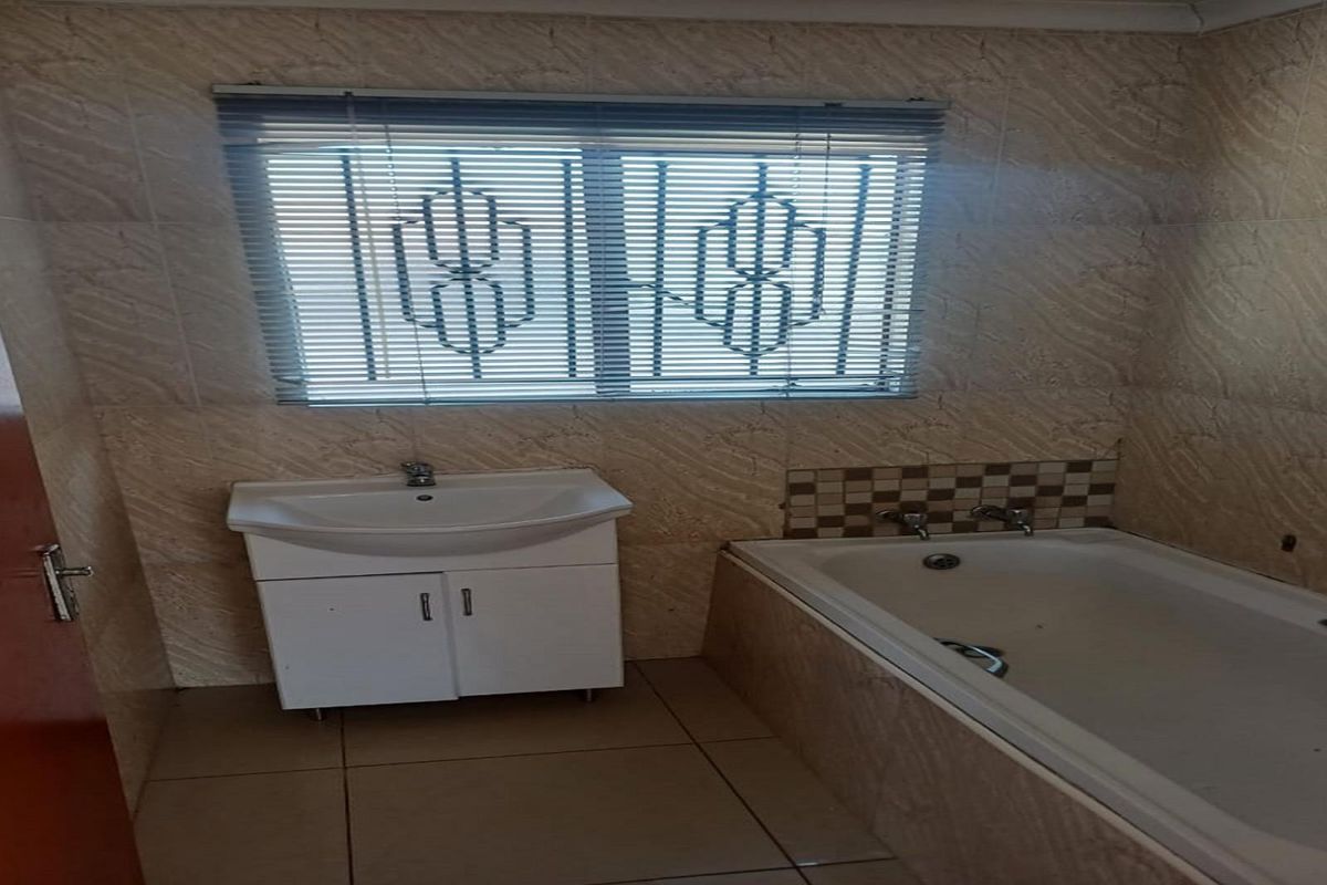 A functional bathroom featuring a built-in bathtub, vanity basin, and tiled walls with security bars on the window.