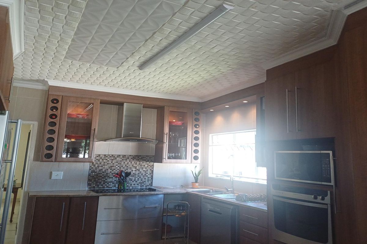 A functional kitchen featuring wood-finish cabinetry, stainless steel appliances, a mosaic tile backsplash, and a distinctive textured ceiling.