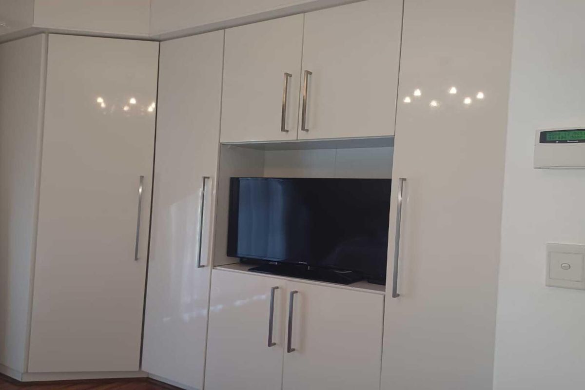 A bedroom featuring modern, high-gloss white built-in cabinetry with integrated storage and a dedicated media alcove.
