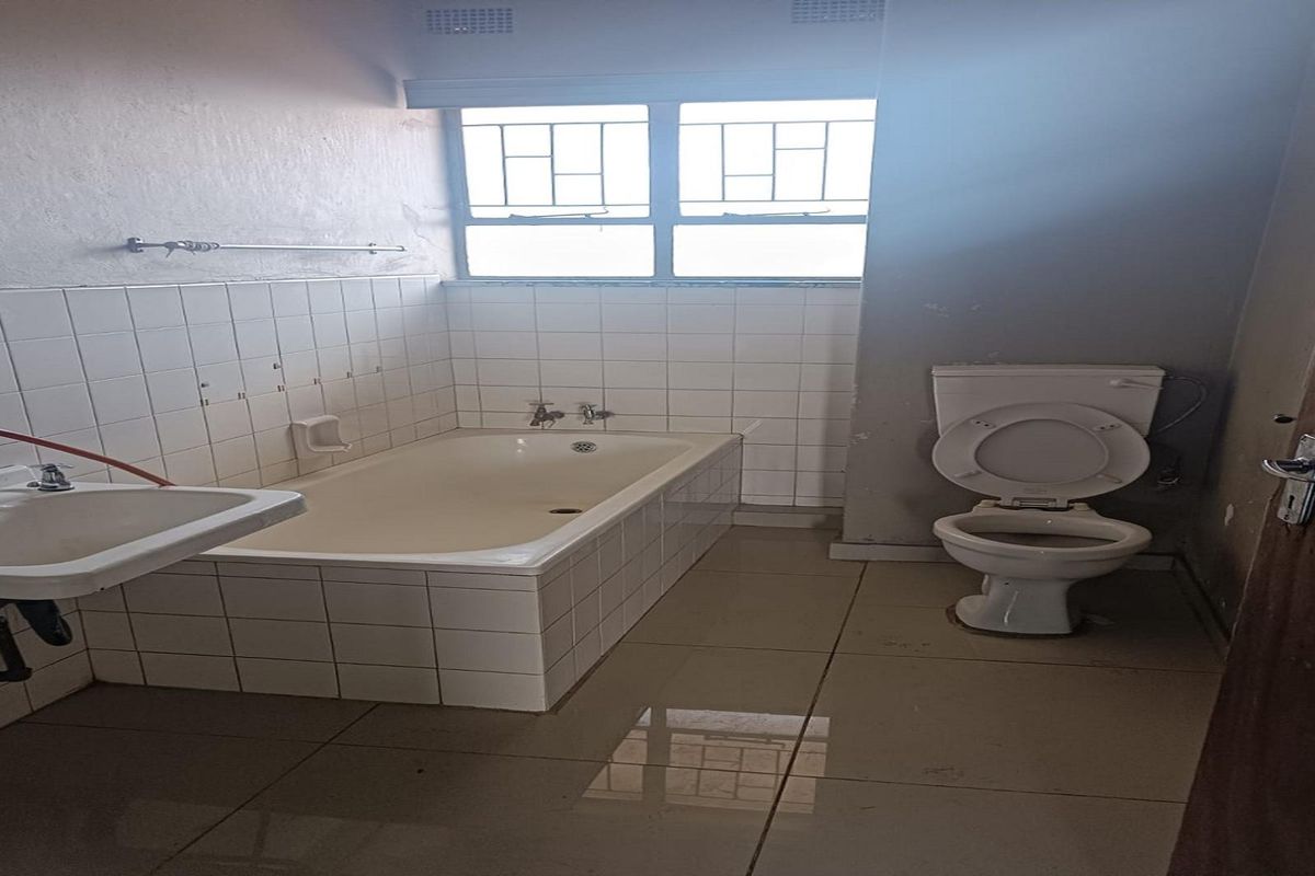 A dated bathroom featuring a built-in bathtub with tiled surround, a pedestal basin, and a standard toilet, requiring cosmetic updates.