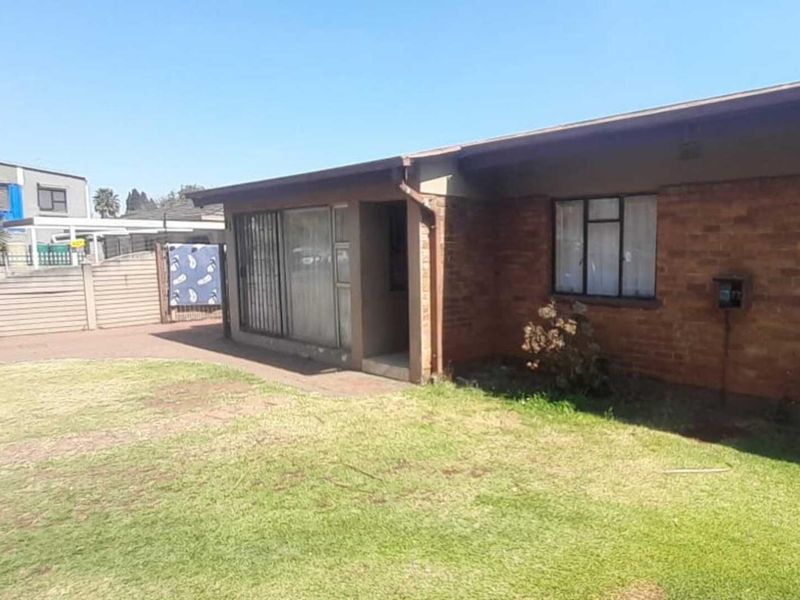 Rear view of a face brick house featuring a sliding door entrance, paved walkway, and a surrounding precast concrete boundary wall.