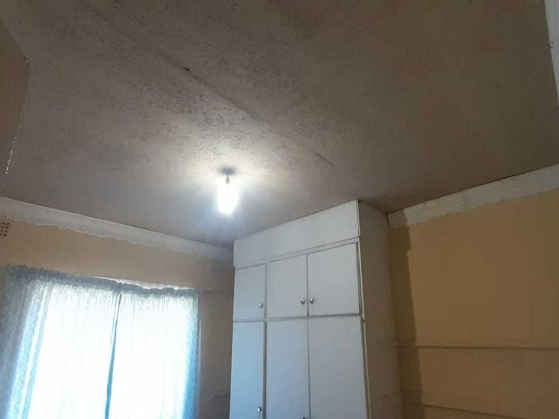 A vacant bedroom featuring built-in cupboards and a ceiling with visible staining, requiring cosmetic updates to improve its overall condition.