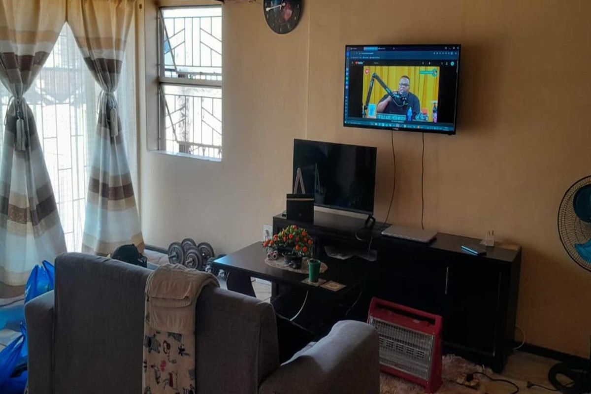 A living room area featuring tiled flooring and windows fitted with security bars, providing a functional space for relaxation.