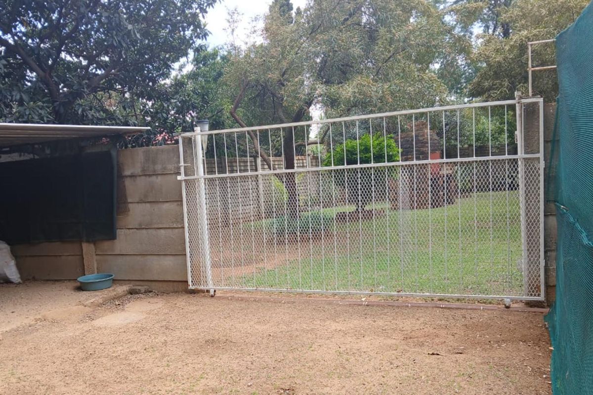 A view of the rear garden area featuring a sliding metal security gate, concrete boundary walling, and established trees.