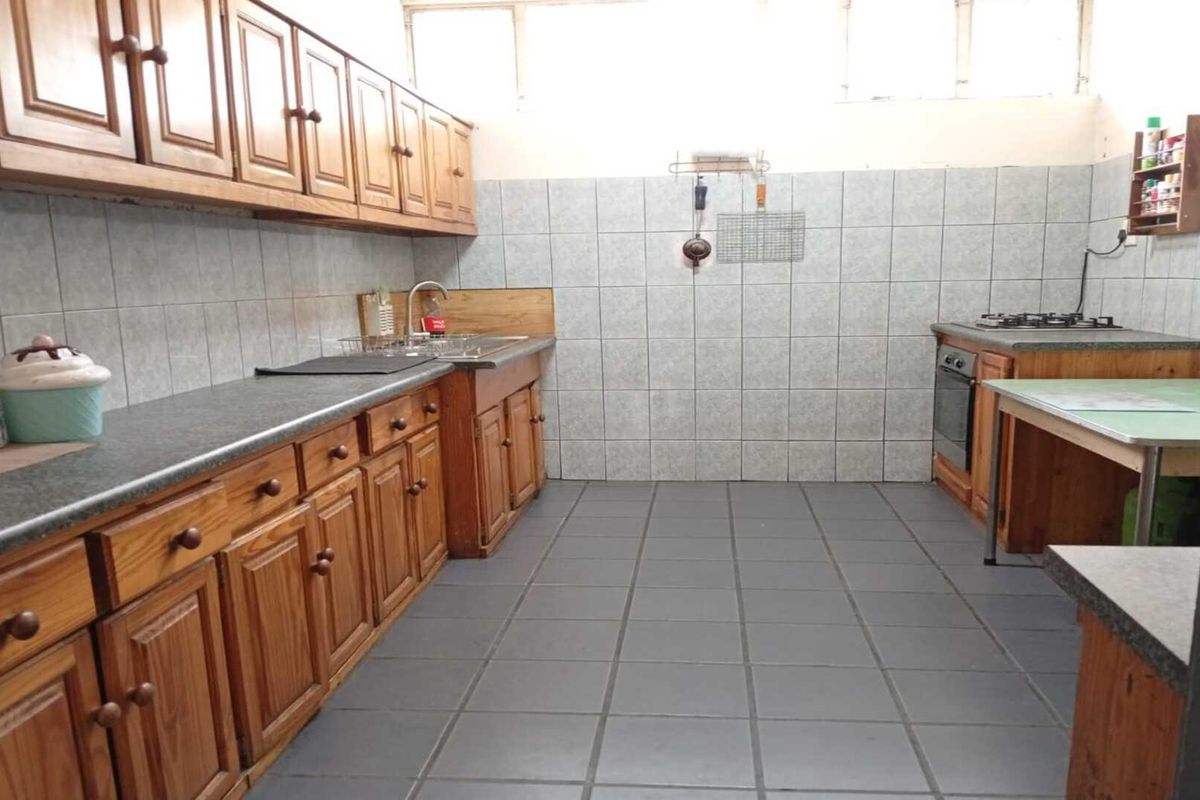 A functional kitchen featuring wooden cabinetry, tiled splashbacks, a built-in oven and hob, and tiled flooring.