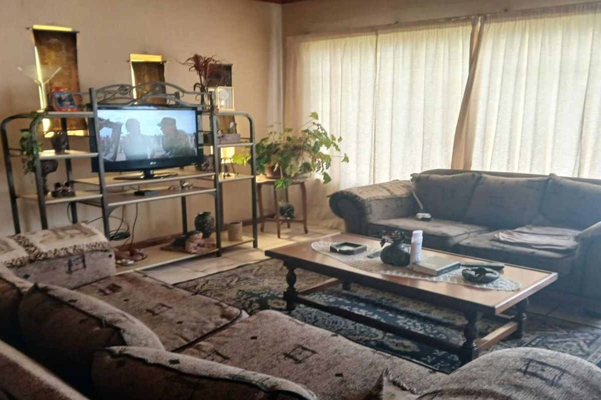 A comfortable living room featuring large windows with curtains, tiled flooring, and neutral wall finishes, providing a functional and inviting space.