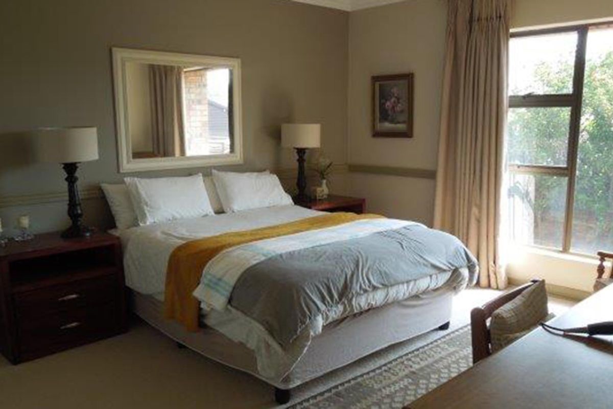 A well-lit bedroom featuring neutral wall tones, large windows with curtains, and a classic layout suitable for a comfortable living space.