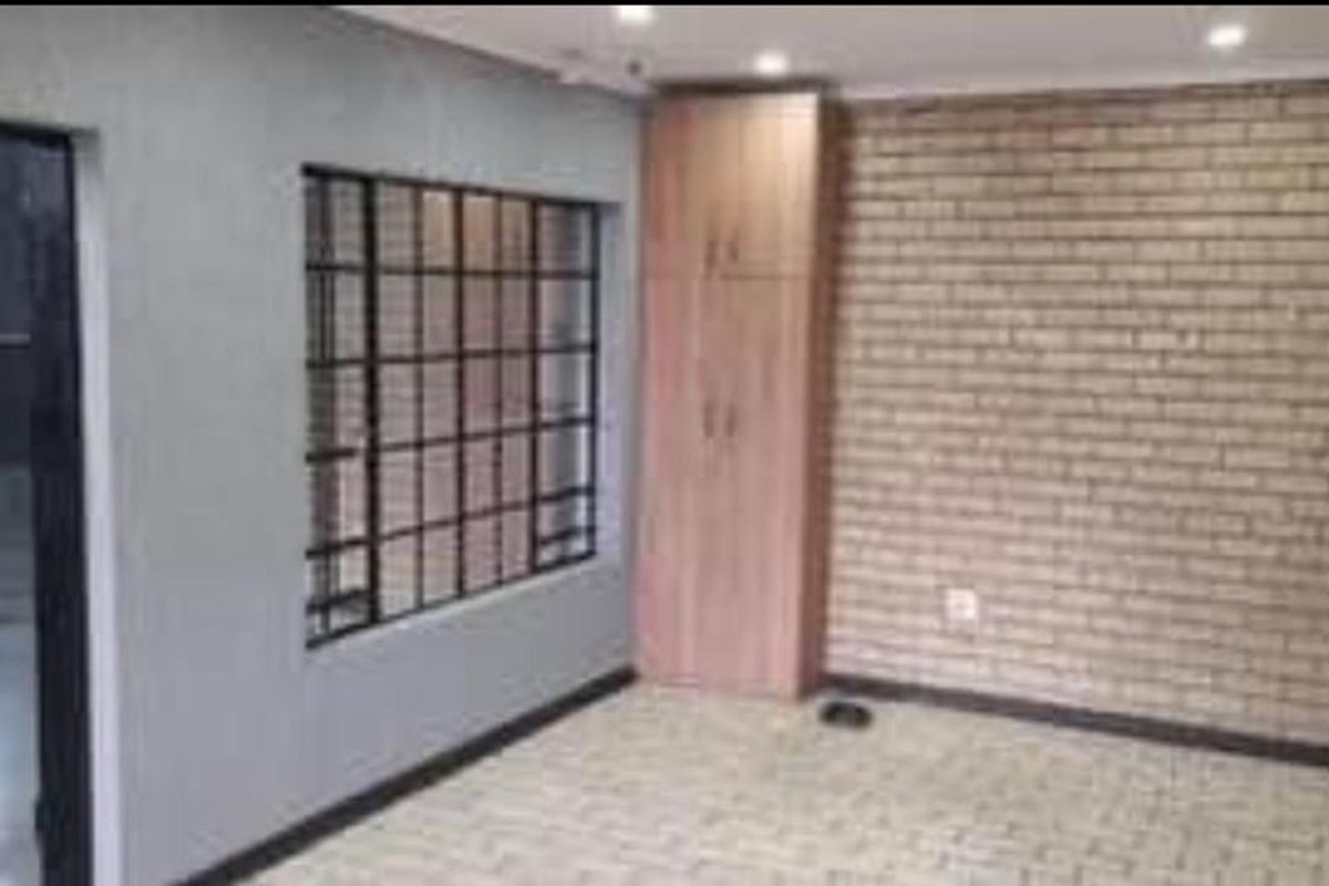 A living area featuring a textured brick feature wall, built-in wooden cabinetry, and a window with security bars.