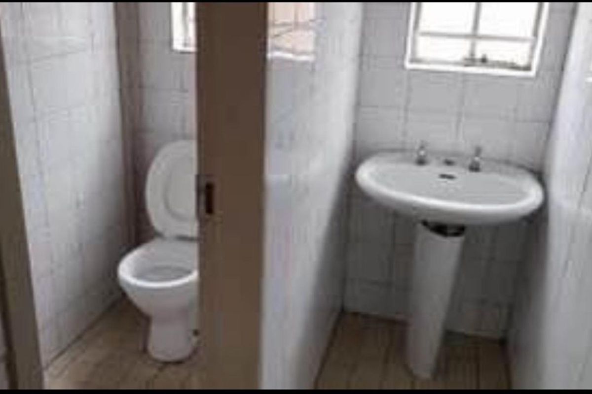 A functional bathroom featuring a pedestal basin and a separate toilet area with white wall tiles throughout.