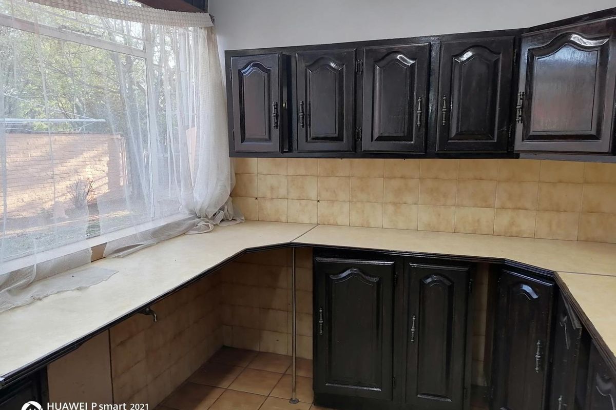 A dated kitchen area featuring dark painted cabinetry, tiled backsplash, and expansive laminate countertops with a large window overlooking the exterior.