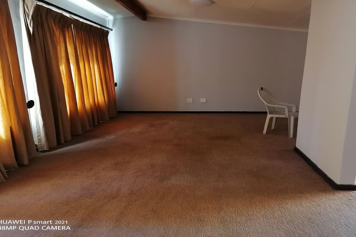 A spacious, empty living room featuring wall-to-wall carpeting and large windows with curtains, offering a blank canvas for potential renovation.
