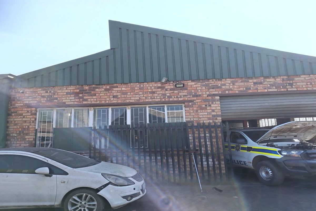 Front exterior view of a brick building featuring a pitched metal roof, security fencing, and a roller shutter garage door.
