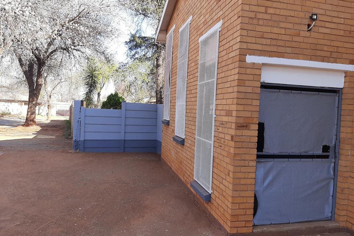 Exterior view of the apartment building featuring face brick walls, security mesh window screens, and a side entrance with a protective door covering.