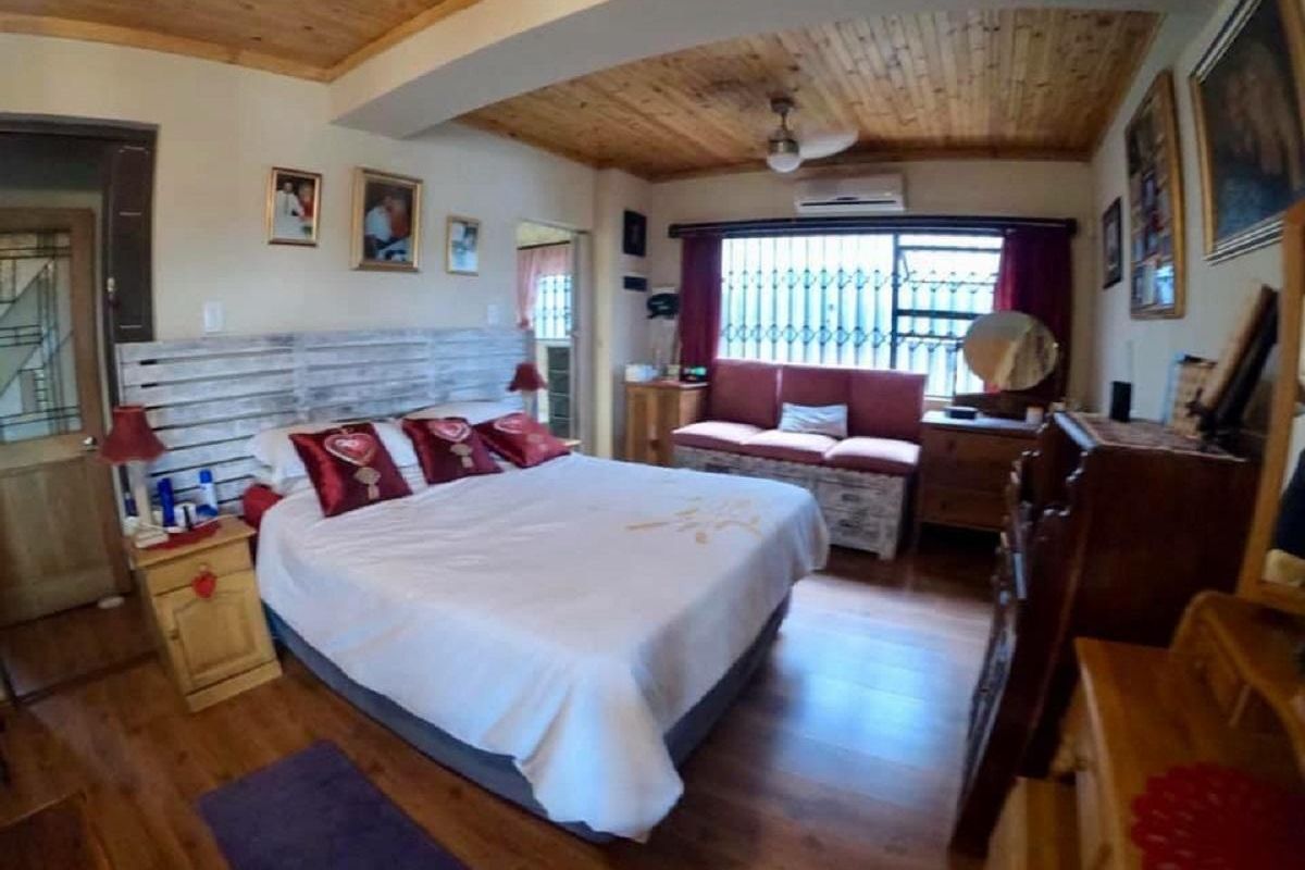 A spacious bedroom featuring warm timber ceiling paneling, wood-look flooring, and a wall-mounted air conditioning unit.