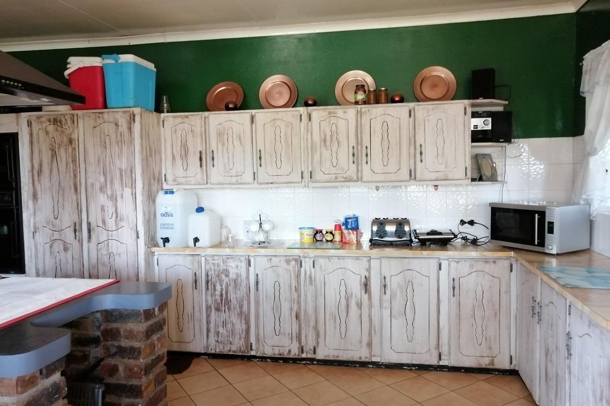A rustic-style kitchen featuring distressed white cabinetry, tiled backsplash, and a brick-based breakfast counter.