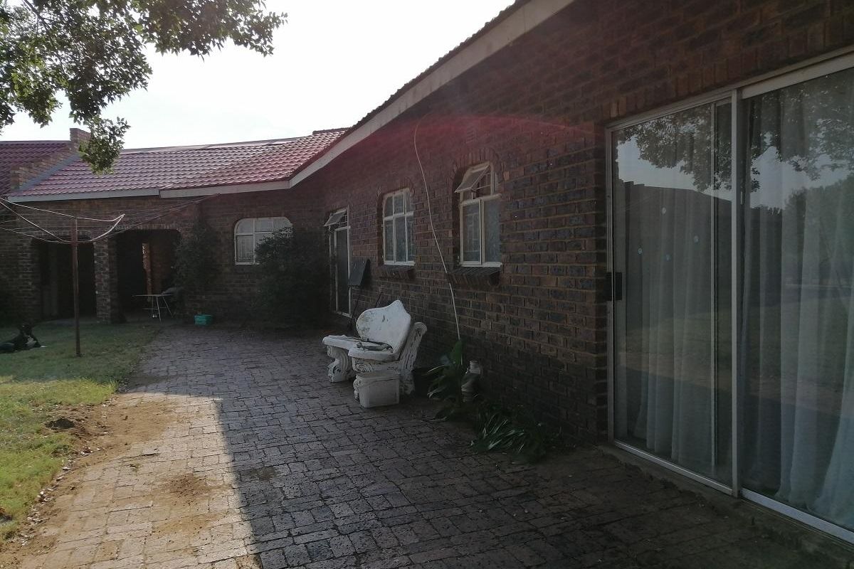 Rear exterior view of the farm property featuring a brick facade, paved patio area, and sliding glass doors leading into the home.