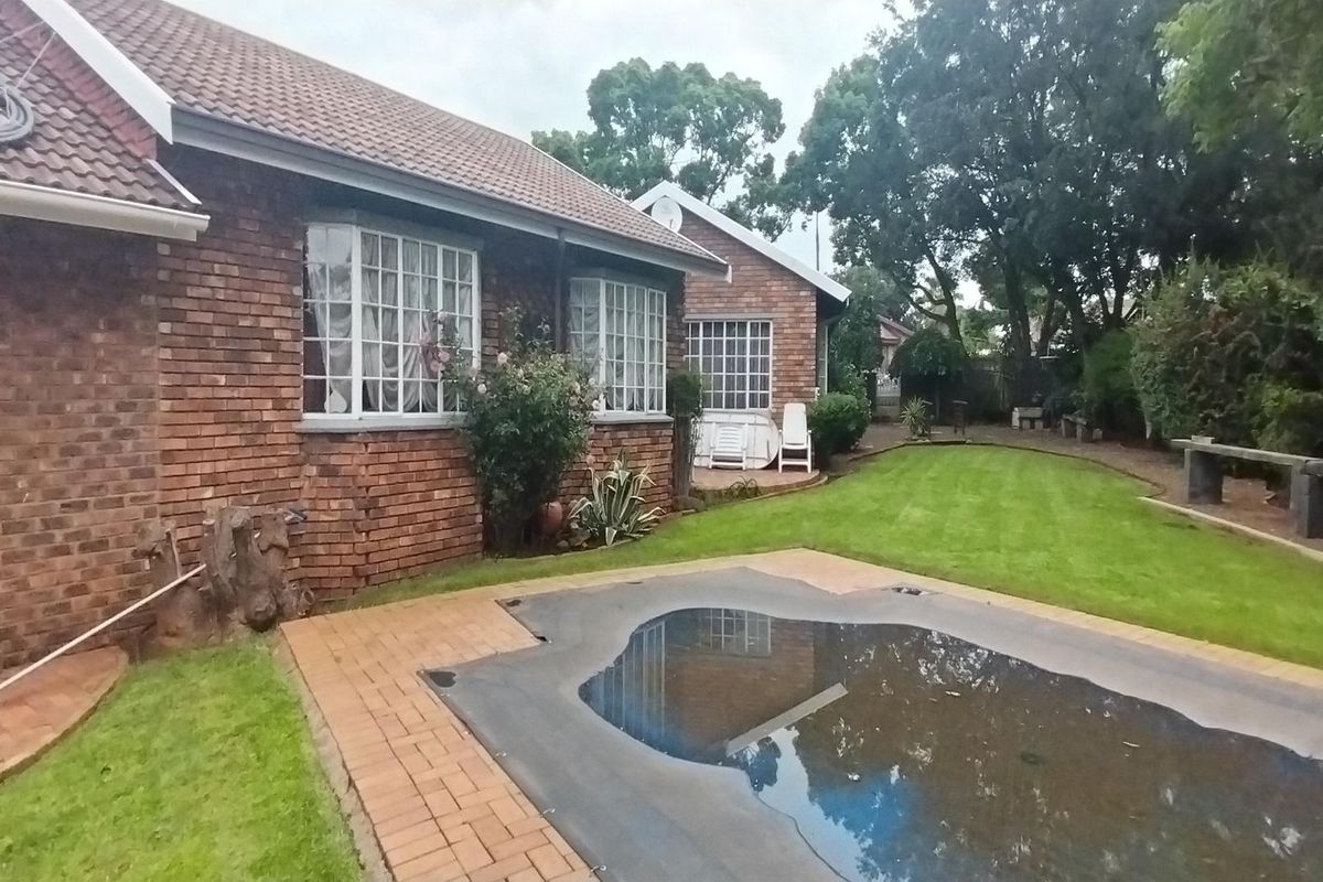 Rear view of the property featuring a brick facade, a swimming pool with a cover, and a landscaped garden area.