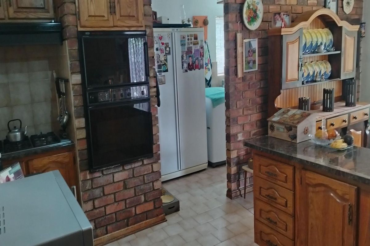 A rustic kitchen featuring exposed brick walls, wooden cabinetry, built-in oven, and a breakfast counter with stone-look countertops.